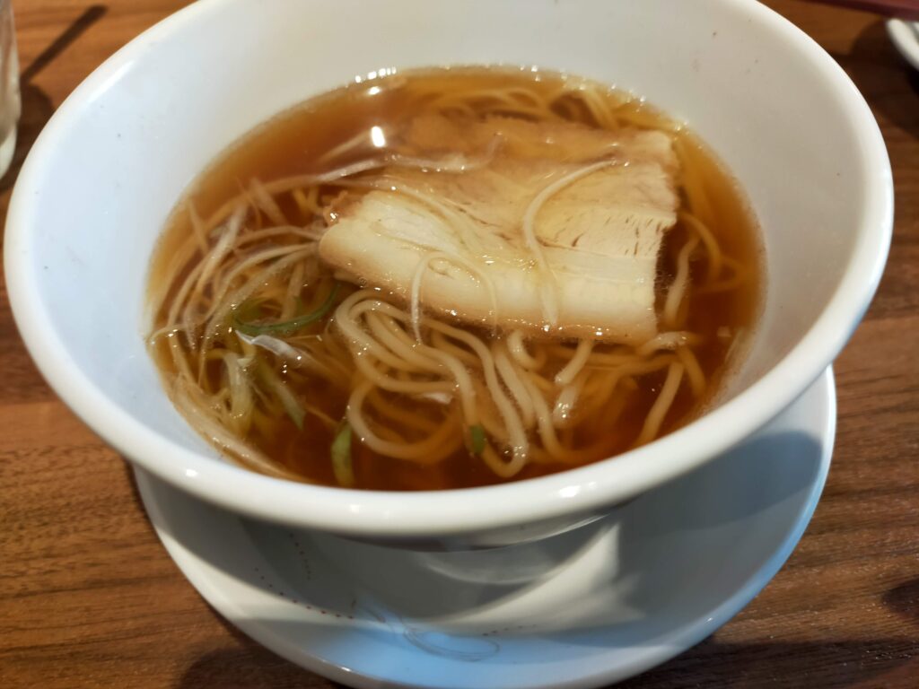 白い器に盛られた醤油ベースのスープと細麺、具材が入った桃菜の中華麺のクローズアップ写真