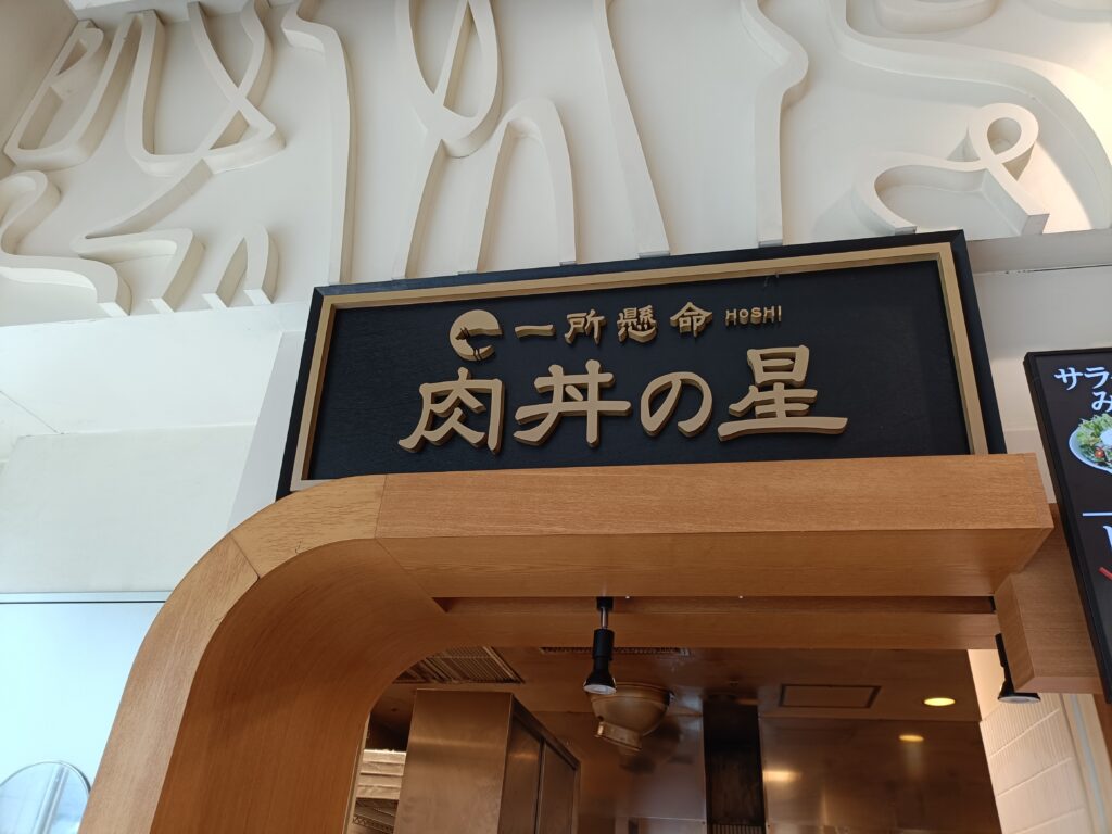 上部に黒地金文字の「肉丼の星」の看板があり、木目の壁と入口が見える店舗外観の写真