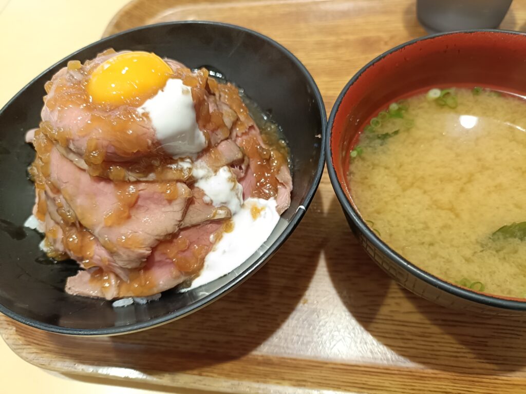 温泉卵をのせた豚肉の丼と、横に添えられたみそ汁の椀がトレーに並ぶ肉丼の星のセットメニューのテーブル写真
