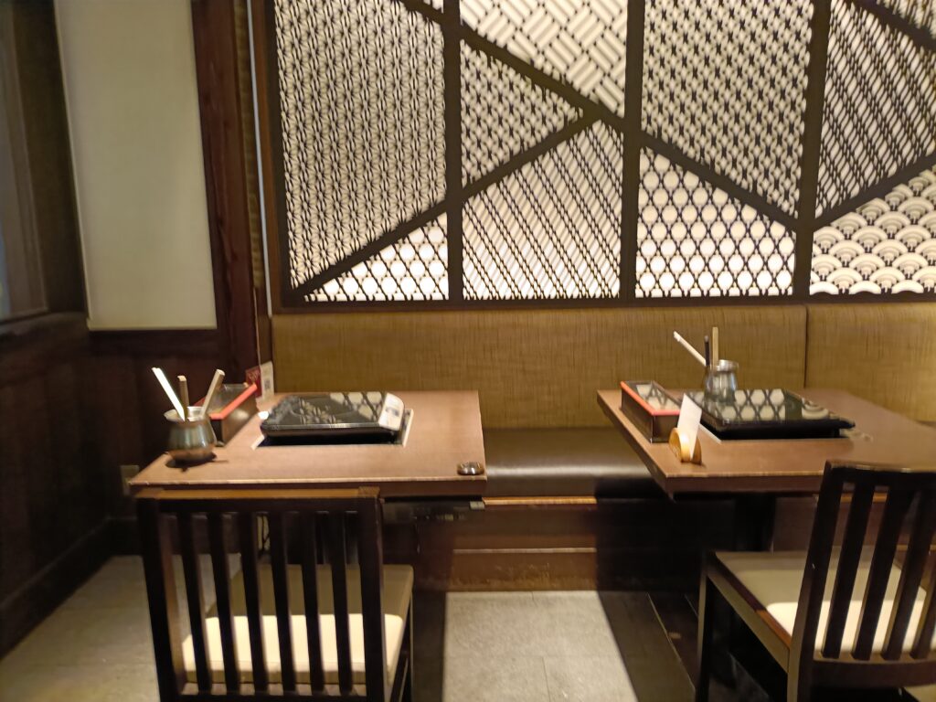 木目調のテーブルと椅子、仕切りのある菜の庵のテーブル席。鍋とタレ、小皿が並んでいる様子。