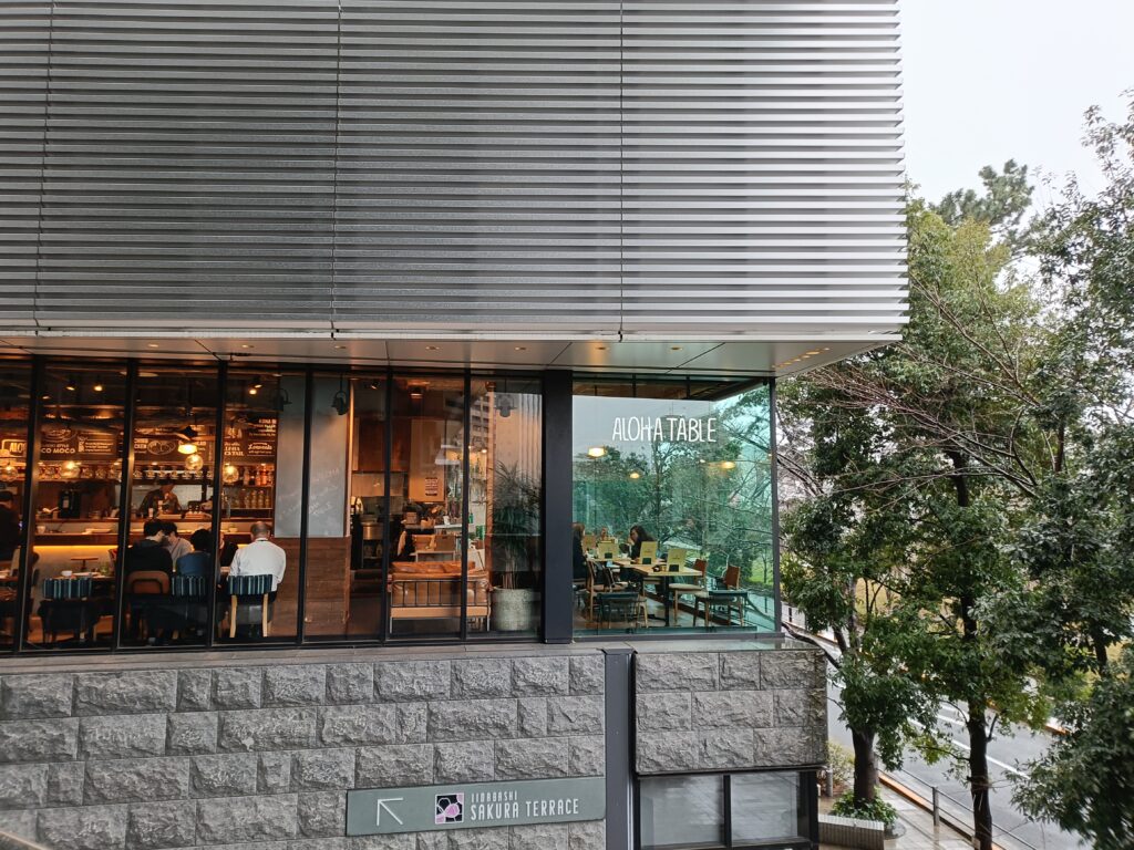 ビル1階にあるアロハテーブルの店舗外観。大きな窓と緑の植栽が見える写真。