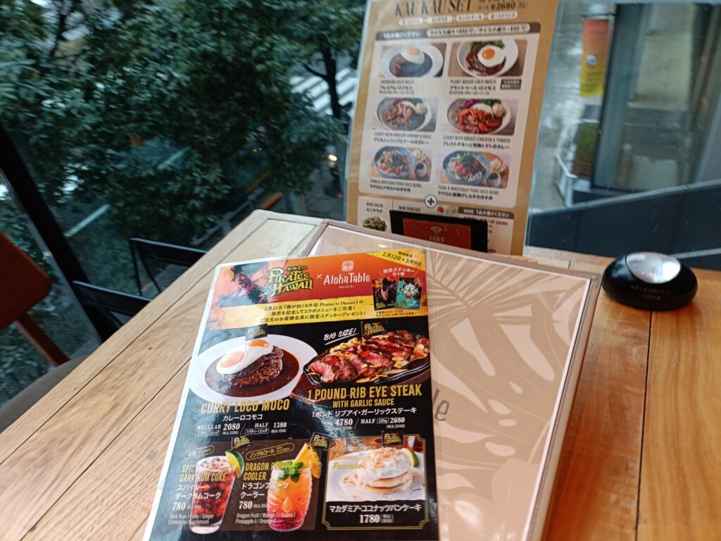 テーブルの上に開かれたアロハテーブルのメニュー冊子のアップ。ハワイアンフードの写真が並んでいる。