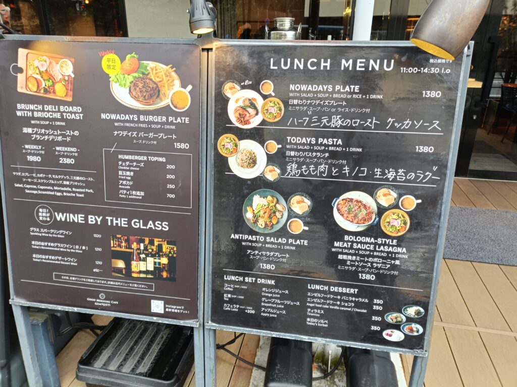 「グッドモーニングカフェの店頭に出されたランチメニュー黒板。パスタやお肉プレート、バーガーなどの写真と価格が並ぶスタンド看板」