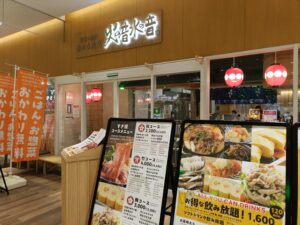 「火の音水の音 さいたま新都心店の店頭外観。木目調の入口前に、すき焼き定食などの写真付きメニューボードが並んでいる様子」