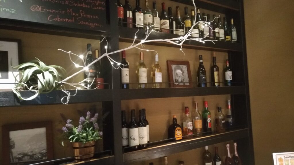 「サルバトーレのバーカウンター背面にワインやスピリッツのボトルがぎっしり並び、ライトが飾られている様子」