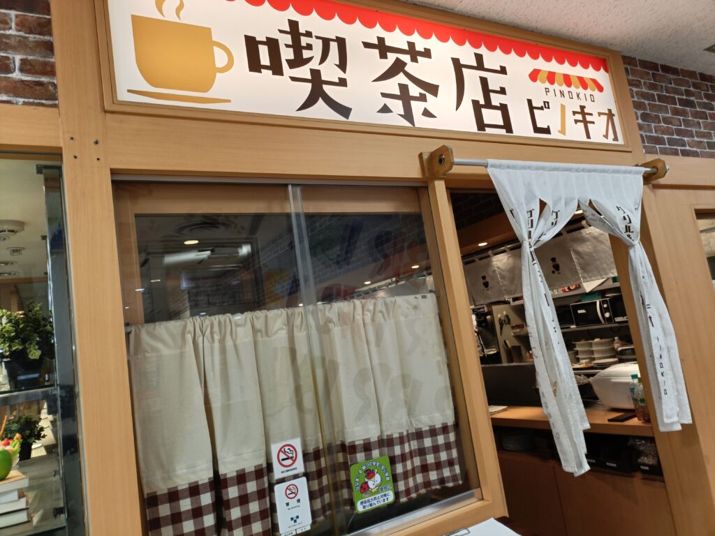 「『喫茶店ピノキオ』と書かれた看板と木枠の窓が並ぶレトロな外観。店内のカウンターやショーケースが見える」
