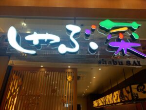 「ショッピングモール内にあるしゃぶ菜の入口。上部に白く光るしゃぶ菜ロゴ看板があり、店内の明かりが外まで漏れている」