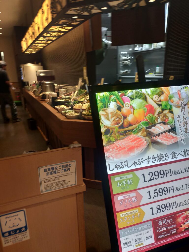 「しゃぶ菜の食べ放題コースの写真付きメニュー看板と、その奥に見える店内カウンターやキッチンの様子」