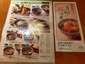「銀座木屋のランチメニュー表。うどんと丼のセット写真が並び、右側に季節限定の桜海老うどんのポスターが印刷されている」
