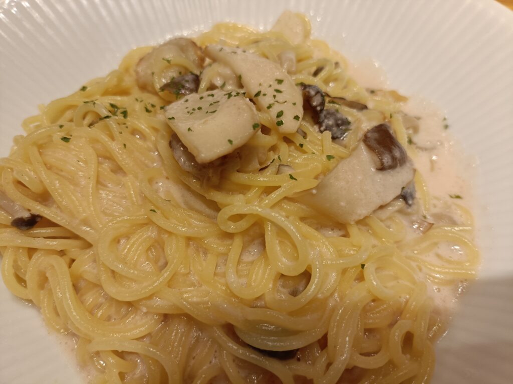 「白い皿に盛られた、角切りきのこがのったクリームソースパスタのクローズアップ」