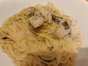 「白い皿に盛られた、角切りきのこがのったクリームソースパスタのクローズアップ」