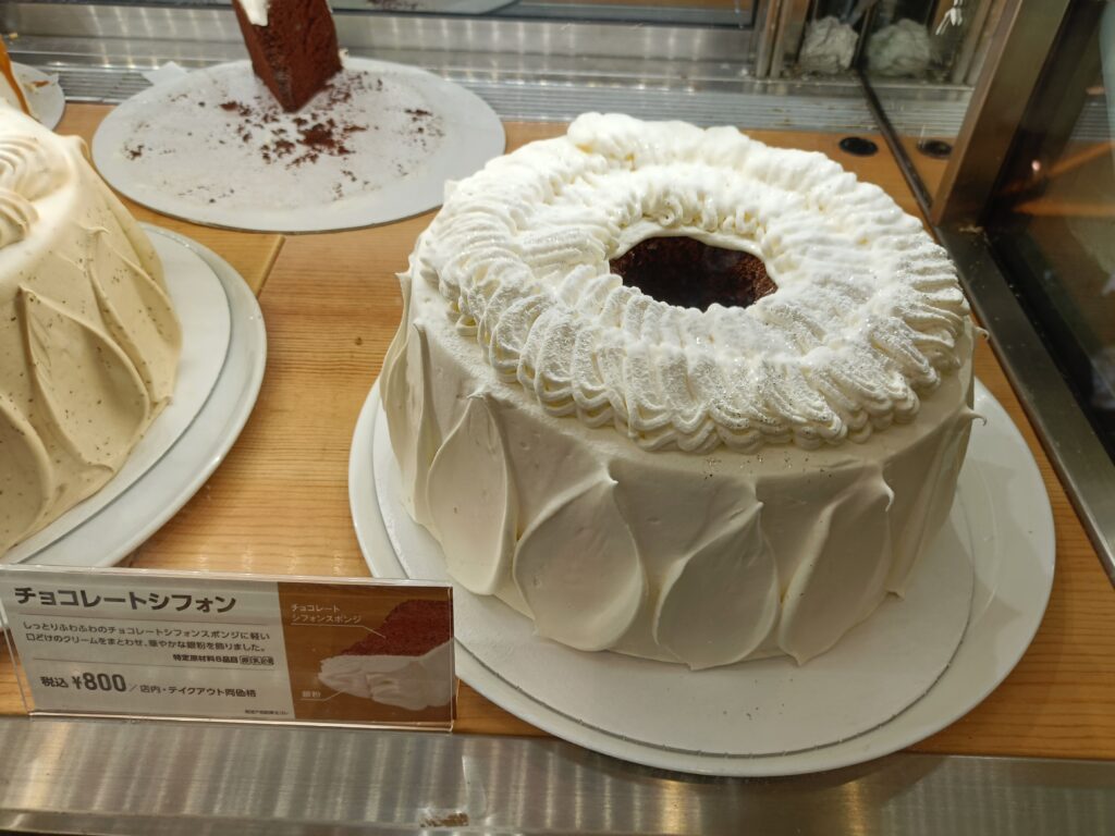 「ショーケース上の台に載せられた、白い生クリームでデコレーションされた丸いシフォンホールケーキ」