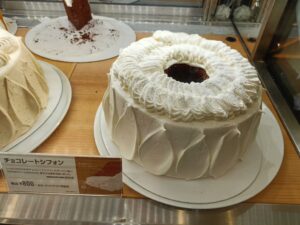 「ショーケース上の台に載せられた、白い生クリームでデコレーションされた丸いシフォンホールケーキ」