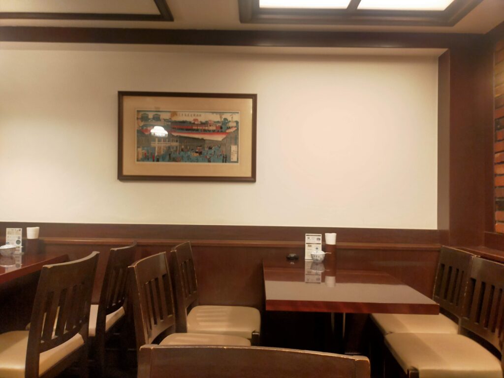 「木製テーブルと椅子が並び、白い壁に絵画が掛けられた椿屋珈琲店内のテーブル席」