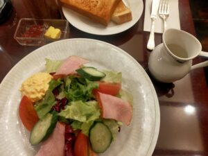 「ハムと野菜が盛られたサラダプレートと、奥にトーストとコーヒーカップが見える椿屋珈琲のモーニングセット」