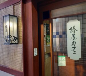 「タイル張りの壁と木の扉に『椿屋カフェ』の文字が入ったガラス看板がかかる、椿屋カフェ渋谷店の入口外観」