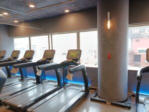 窓際に並ぶトレッドミル（ランニングマシン）。明るい室内で有酸素運動ができるジムエリア。