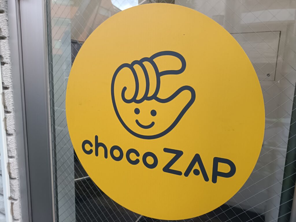 chocoZAPの黄色い円形ロゴ看板。入口付近に掲示された店舗サイン。