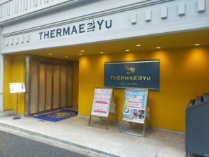 「白い外壁にTHERMAE YUのロゴと金色の看板が並ぶ、テルマー湯 西麻布の入口外観」