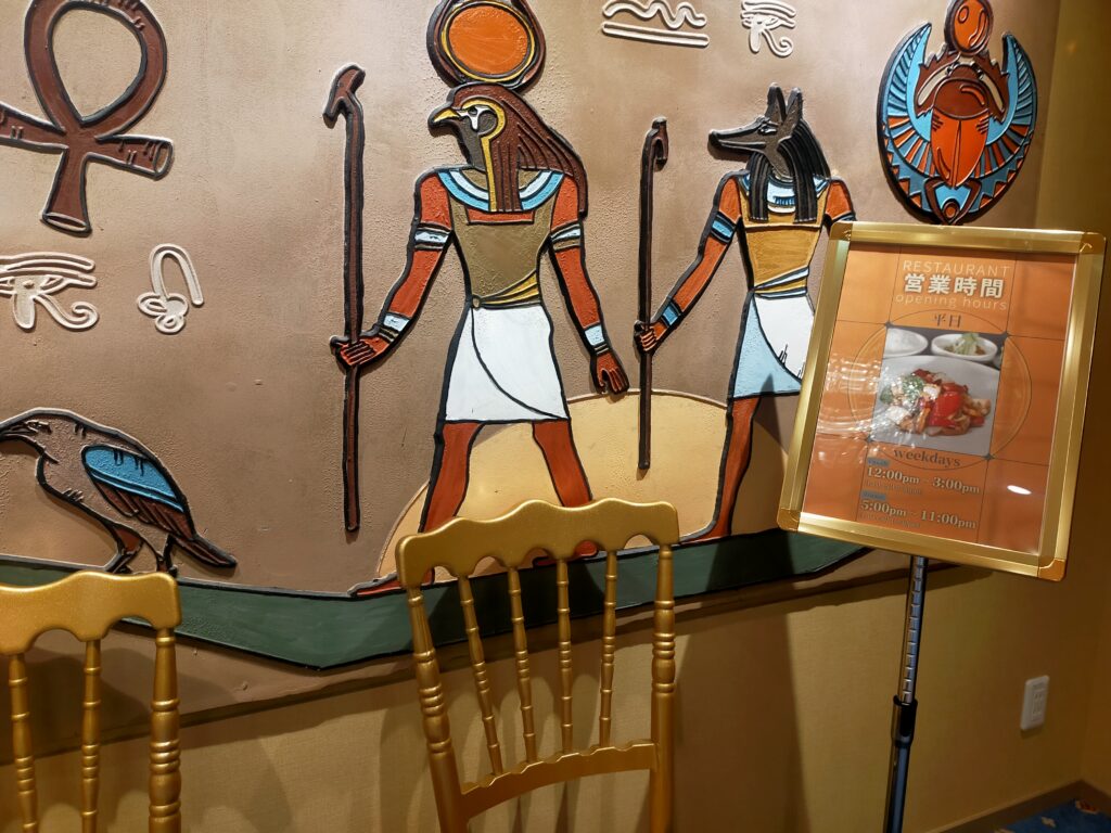 「エジプトの神を描いた壁画と金色の椅子が配置された、テルマー湯 西麻布のエジプト風ラウンジスペース」