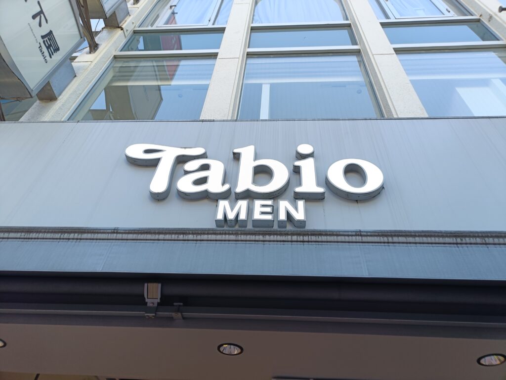 「ビルの1階に『Tabio MEN』のロゴ看板が掲げられたメンズ向け靴下専門店の外観」
