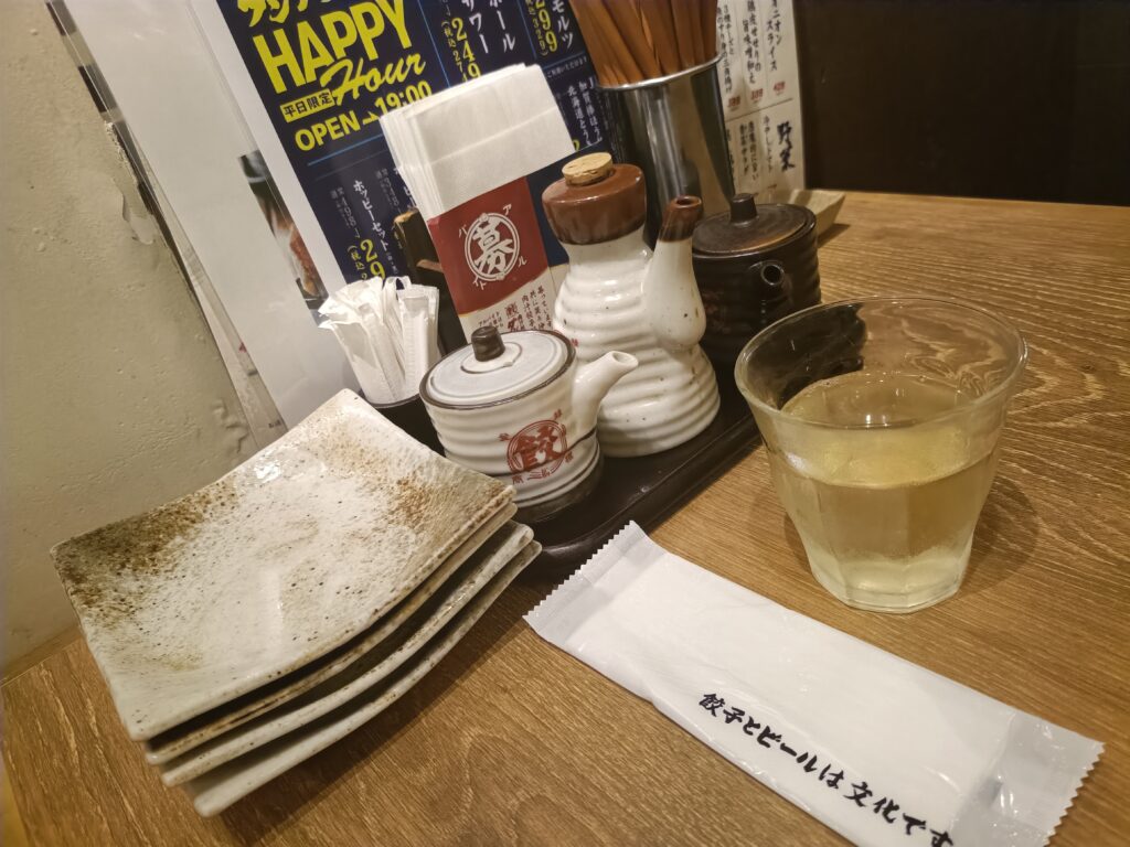 「肉汁餃子のダンダダンのテーブルに並ぶ小皿、箸、餃子のタレや酢・ラー油のボトルとグラスのお冷」