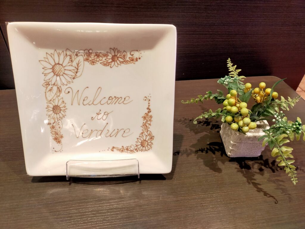 「東武ホテルレバント東京レストラン入口のテーブルに置かれたWelcomeプレートと小さな花のアレンジメント」