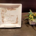 「東武ホテルレバント東京レストラン入口のテーブルに置かれたWelcomeプレートと小さな花のアレンジメント」