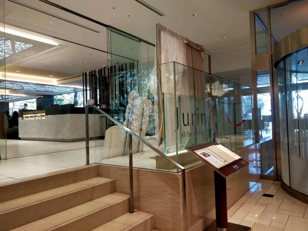 「京王プラザホテル新宿ロビーから続く階段と、ガラス越しに『Glass Court』のロゴが見えるレストラン入口」