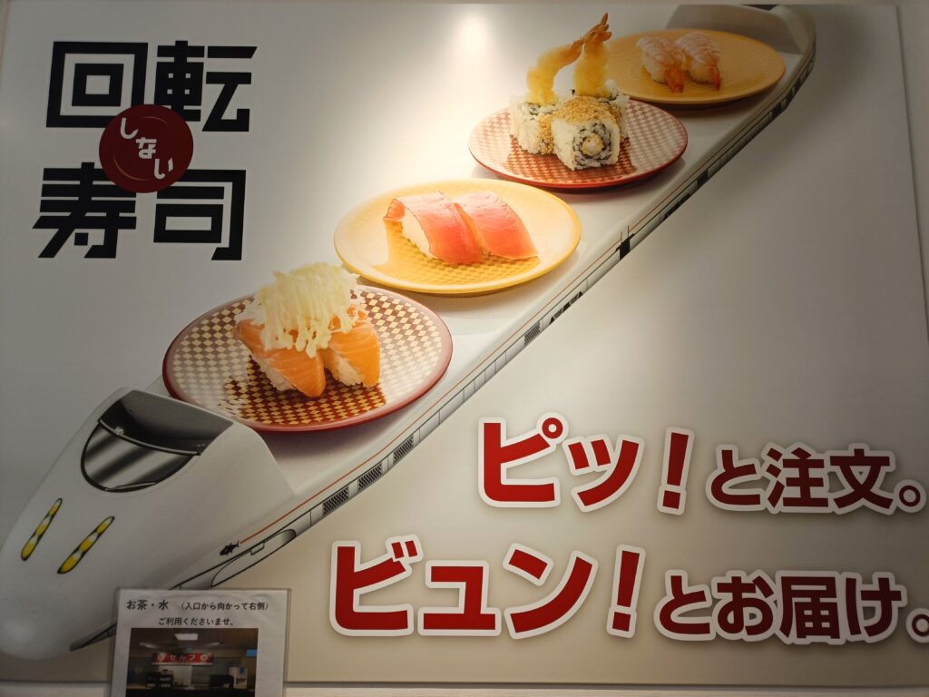 魚べいの店頭ポスター。回転寿司の案内文と寿司の盛り合わせ写真が掲載されている。