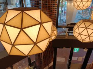 「多面体の和風ペンダントライト越しに下階の通路が見える、chawan阿佐ヶ谷店の吹き抜けフロア」