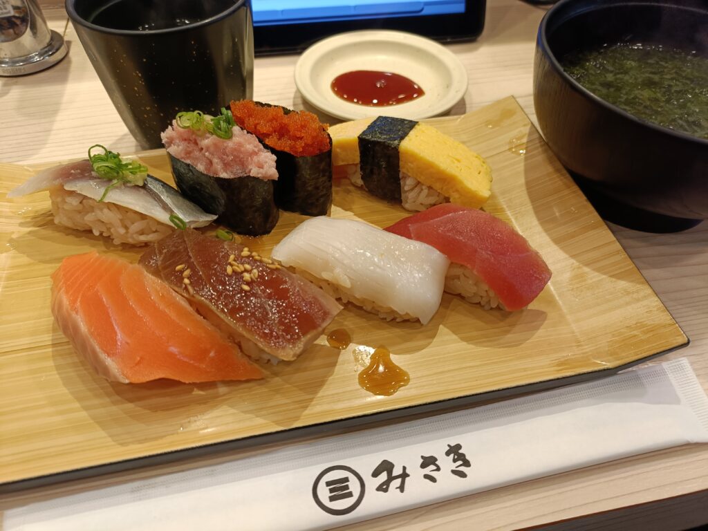 回転寿司みさきで提供される、複数のにぎり寿司が木の板に並び、味噌汁と小鉢が添えられたランチセットのテーブル写真