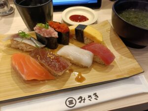 回転寿司みさきで提供される、複数のにぎり寿司が木の板に並び、味噌汁と小鉢が添えられたランチセットのテーブル写真