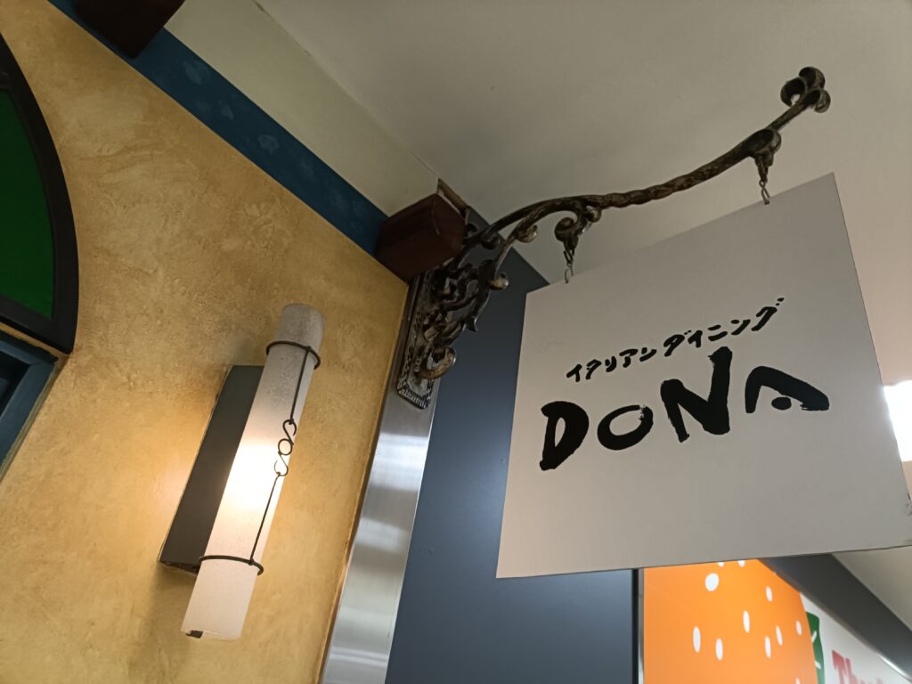 イタリアンダイニングDONAの店頭看板とロゴが見える入口付近の様子