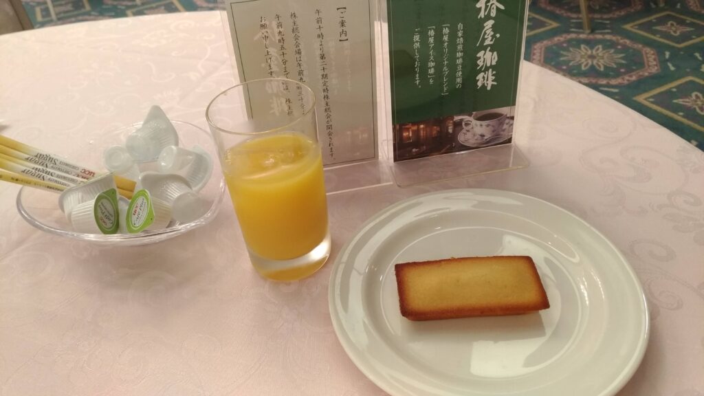 オレンジ系ドリンクと小さなスイーツが皿に盛られた株主総会前のドリンクサービス風景