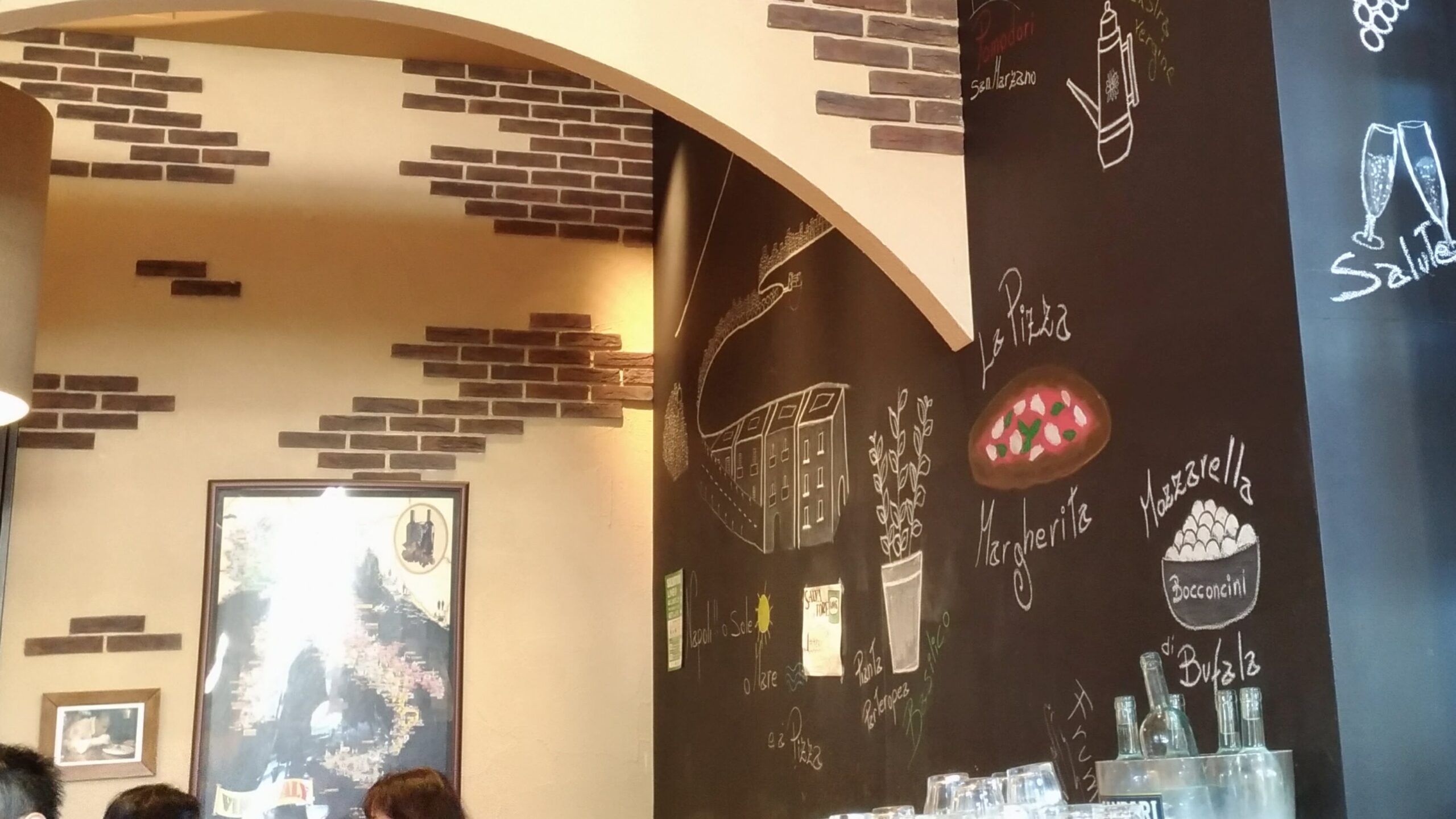 「レンガアーチと黒板アートがあるサルバトーレ店内入口。壁にはピザやワインのイラストとメニューが描かれている」