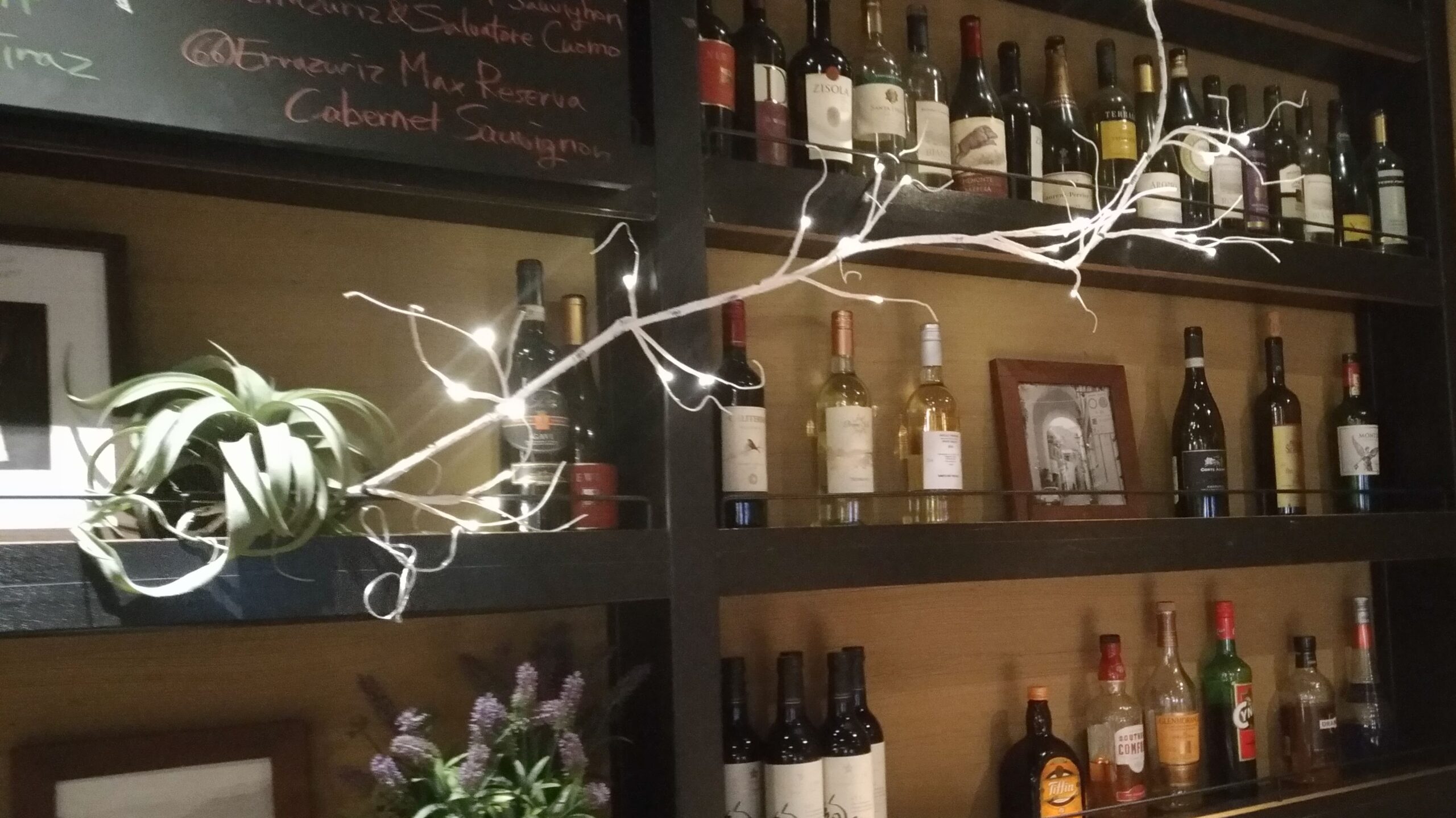 「サルバトーレのバーカウンター背面にワインやスピリッツのボトルがぎっしり並び、ライトが飾られている様子」